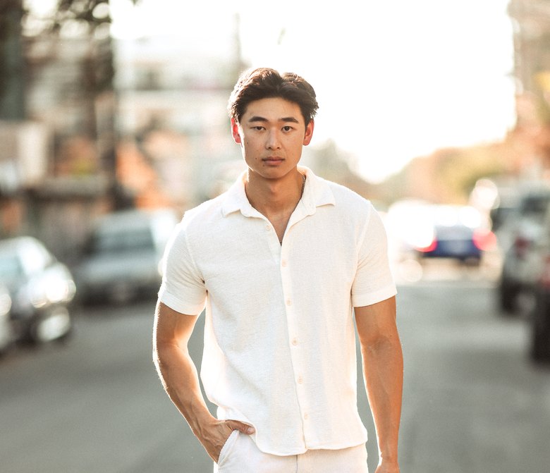 Scott Ho in Bali, sunglasses on, standing against a wall of jungle leaves